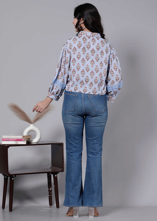 Woman wearing a floral blouse and blue jeans standing in front of a small table with decor items.