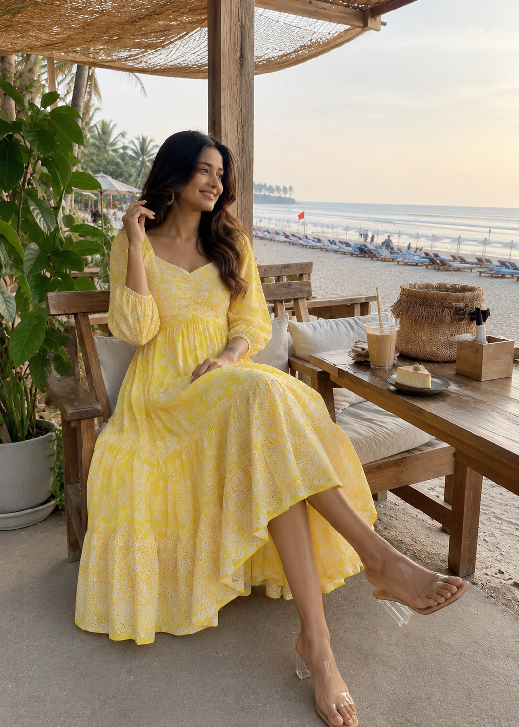 Woman in a yellow dress sitting at a beachside table with a scenic view.