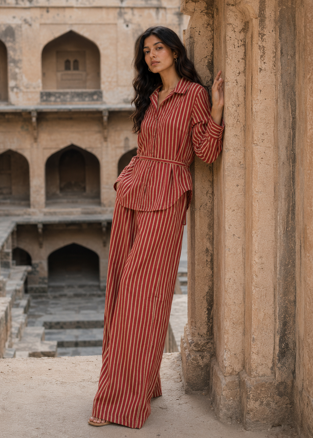 Woman in a red striped outfit standing in front of an ancient architectural structure.