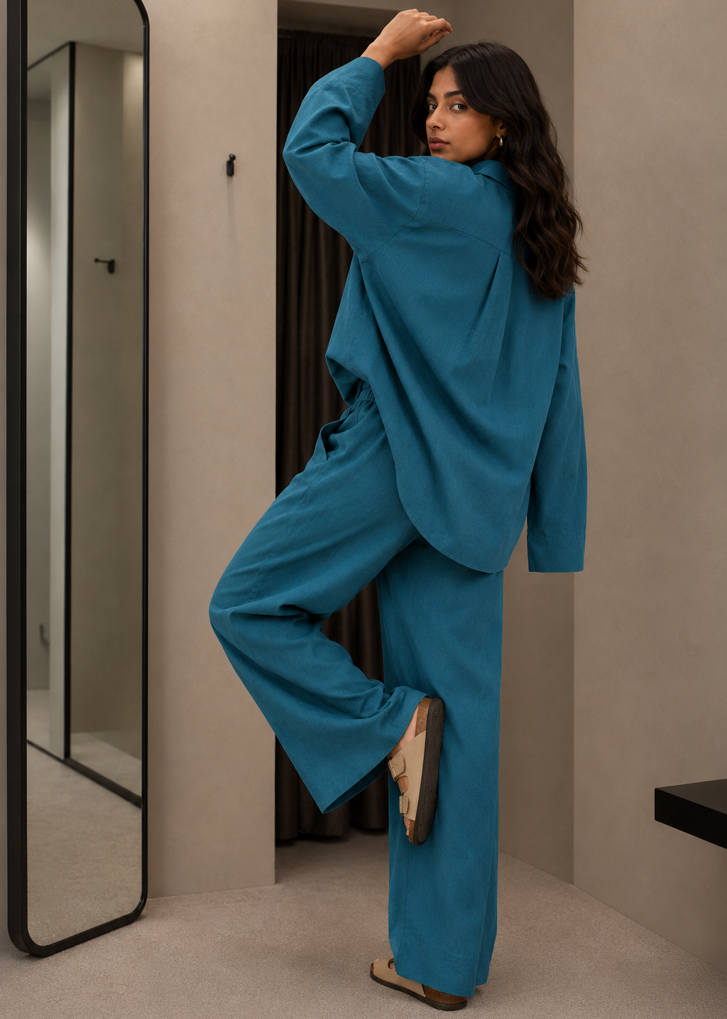 Woman in a blue outfit standing in front of a mirror in a room.